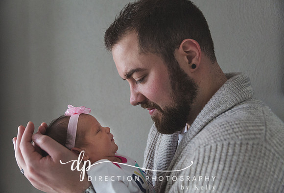A young father cradling the head of his newborn daughter